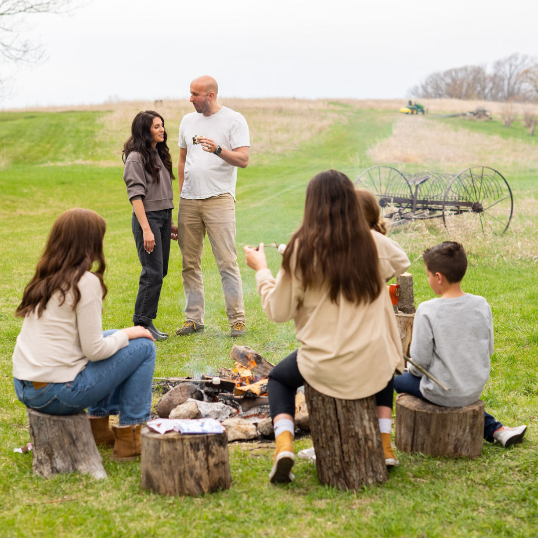 Family and friends gathered around a campfire in a field.